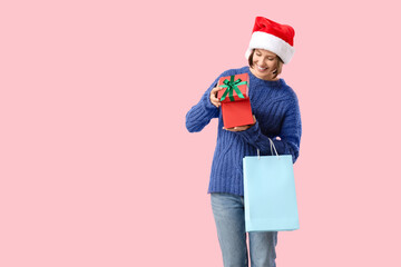 Beautiful young happy woman in Santa hat with shopping bag and gift box on pink background. Christmas celebration