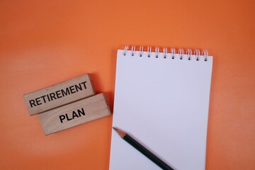 Blank notebook, pencil, and wooden blocks spelling retirement plan set against a bright orange background, symbolizing planning, finance, and future goals.