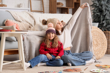Cute sisters in warm hats with plaid at home on Christmas eve