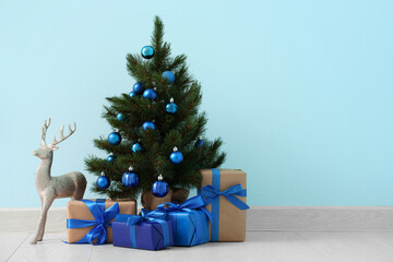 Beautiful Christmas tree with gift boxes and reindeer near blue wall in room