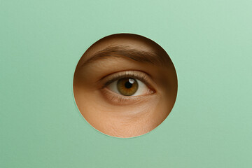 Close up view of eye peering through circular cutout in green paper, creating striking visual effect. image conveys curiosity and intrigue, highlighting eye details and texture