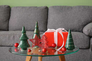 Christmas balls with toy fir trees and gift box on table in living room, closeup
