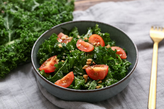 Bowl of tasty kale salad with tomatoes, walnuts and fork on napkin