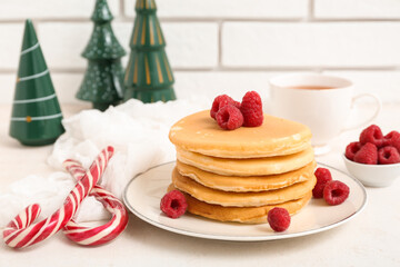 Plate of sweet pancakes with raspberries, candy canes, cup of tea and Christmas trees on white table