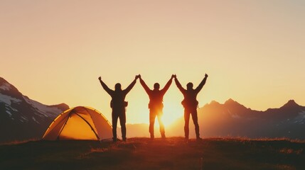 Fototapeta premium Three hikers with backpacks celebrating their arrival at a remote hilltop camping spot with arms raised in triumph as the sun sets over the majestic mountain landscape in the background