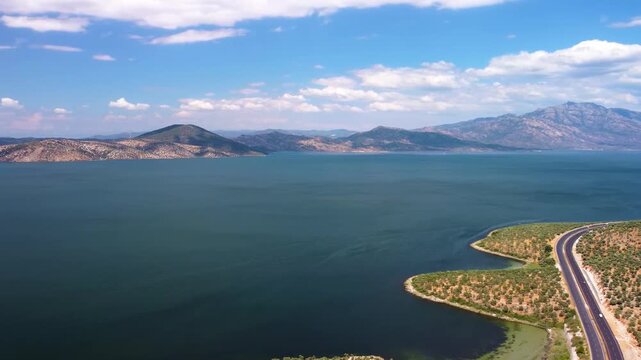 aerial perspective captures the tranquil beauty of Bafa Lake in Turkey, showcasing its vast, deep blue waters, the surrounding lush green vegetation, and the majestic mountainous backdrop under a clea