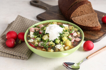 Bowl of tasty okroshka with sour cream, bread and fresh radish on light background