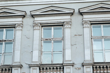 Two old windows on the white facade of a neoclassical building with columns and capitals and decorative elements.