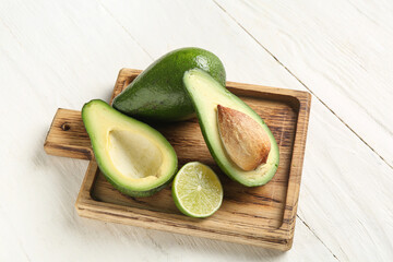 Cutting board with fresh ripe avocados and half of lime on white wooden background
