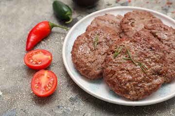 Plate with tasty meat cutlets, cut tomato and peppers on grey grunge background
