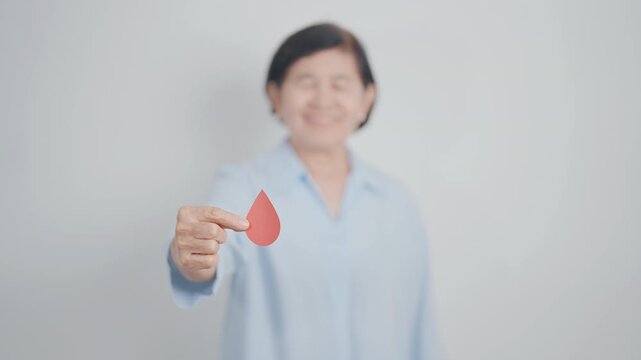 Elderly woman in blue shirt with red Blood drop for World Diabetes Day, Blue November Health month, Diabetes awareness, Blood sugar check, Insulin, Glucose screening, blood donoo and Health checkup - Powered by Adobe