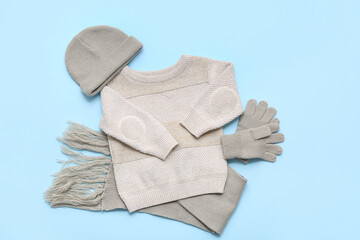 Stylish children's sweater, scarf, hat and gloves on blue background