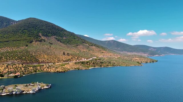 An aerial drone shot captures the serene beauty of Bafa Lake in Turkey, showcasing its clear blue waters, surrounding lush mountains, and the small islands dotted with ancient ruins.