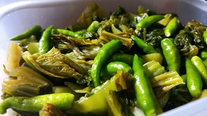 Sliced ​​pickled mustard greens with green bird's eye chilies in a white plastic container, chinese traditional food