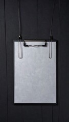 A black clipboard with blank white paper hangs on a dark wooden wall