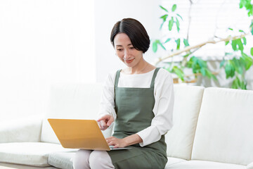 ソファに座りパソコンで仕事をするエプロンをつけた女性
