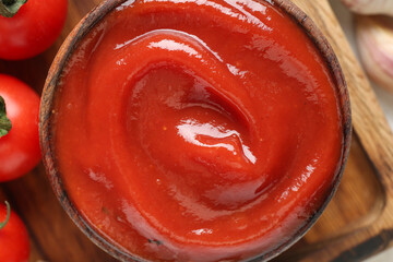 Bowl with tasty ketchup on wooden tray as background, closeup