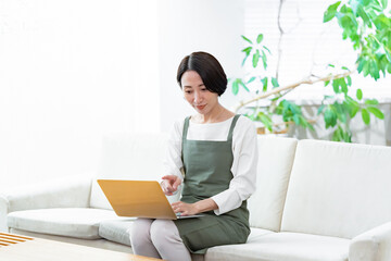 ソファに座りパソコンで仕事をするエプロンをつけた女性