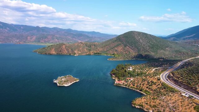 aerial drone shot showcasing the tranquil waters of Lake Bafa, surrounded by lush, rolling hills and mountains under a clear blue sky in Turkey. This footage captures the natural beauty and historical
