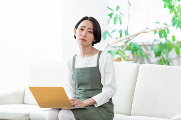 ソファに座りパソコンで仕事をするエプロンをつけた女性