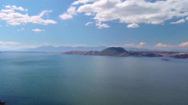 panoramic view capturing the serene beauty of Bafa Lake in Turkey, surrounded by rolling hills and a clear blue sky with scattered clouds. This footage highlights the tranquil waters and natural lands