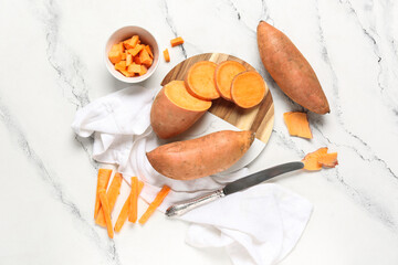Composition with wooden cutting board, knife and fresh sweet potatoes on marble background