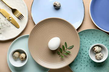Different clean plates with Easter eggs, fresh green leaves and gypsophila flowers on beige background