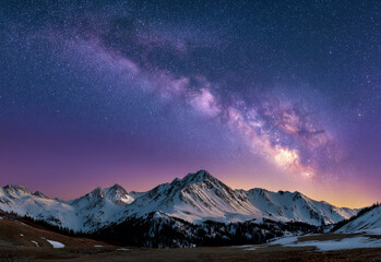 A breathtaking view of the Milky Way galaxy arcing across a clear night sky above a snow-covered mountain range at dusk.