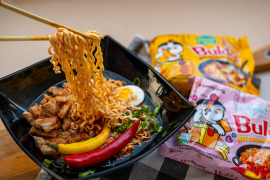 Korean Ramen Buldak noodles with egg, chili and chicken in bowl lifted chopsticks, tasty Authentic Asian street food, Homemade meal, global trend popular food product, Frankfurt - September 30, 2025