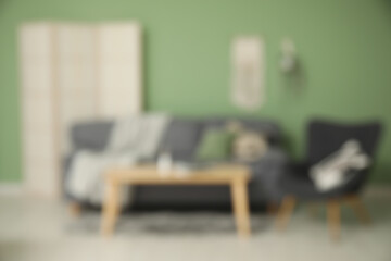 Blurred view of living room with table, sofa and armchair near green wall