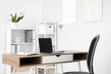 Workplace with blank laptop and lamp in light office
