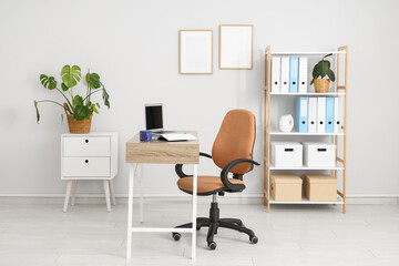 Comfortable workplace with modern laptop near white wall in interior of office