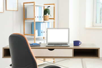 Workplace with modern laptop and cup of coffee on table in interior of office, closeup