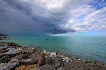 Rocky shoreline with a stormy sky and a boat in the water