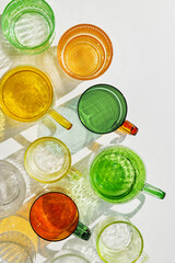 Colored shiny drink Glasses still life with shadow and sunlight reflections on white, minimal aesthetic top view summer photo, refraction at glass cups with sun glare, creative pattern