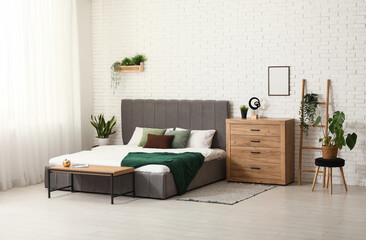 Fototapeta na wymiar Stepladder, houseplants and chest of drawers near white brick wall in interior of bedroom