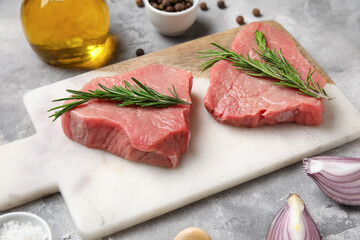 Board with fresh raw steaks and different spices on grey background, closeup