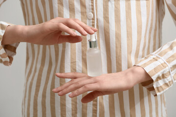 Young woman in pajamas with bottle of serum on white background, closeup