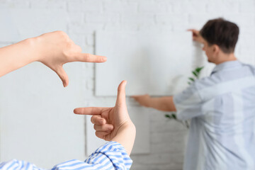 Young woman with her boyfriend hanging painting on white brick wall at home, closeup