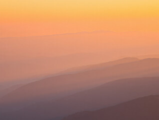 Fototapeta premium A soft gradient sky over hazy mountain ranges with a warm orange and purple color palette at sunrise