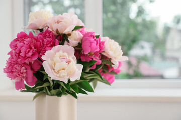 Vase with beautiful peony flowers near window in room, closeup