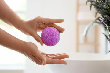 Female hands with bath bomb in interior of bathroom, closeup