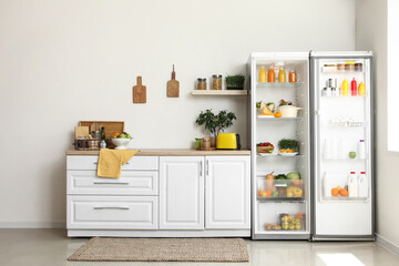 Open big refrigerator with products and white counters in interior of kitchen