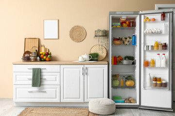 Open big refrigerator with products near beige wall in interior of kitchen