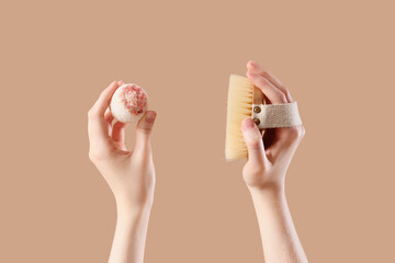 Female hands holding bath bomb and massage body brush on beige background, closeup