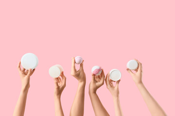 Female hands with bath bombs and jars of cosmetic products on pink background