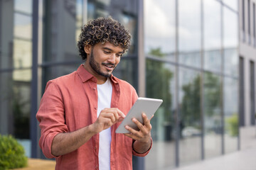 Indian young man in red shirt standing on the street and using tablet