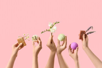 Female hands holding soap bars, bath bombs and flowers on pink background
