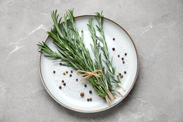 Plate with bunch of fresh rosemary, peppercorns and sea salt on grey background