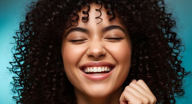 Radiant Smile: A young woman with a vibrant, curly hairstyle closes her eyes in pure joy, her face illuminated by a radiant smile, expressing genuine happiness and inner peace.